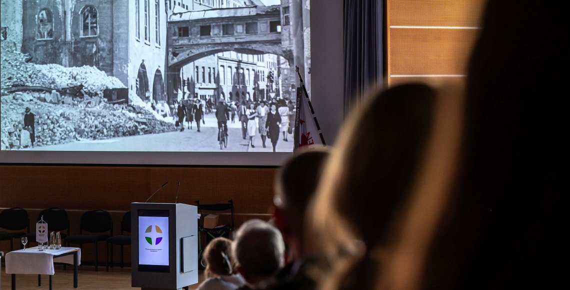 Blick auf eine schwarz-weiße Leinwand, auf die Bilder einer kriegszerstörten Stadt zu sehen sind
